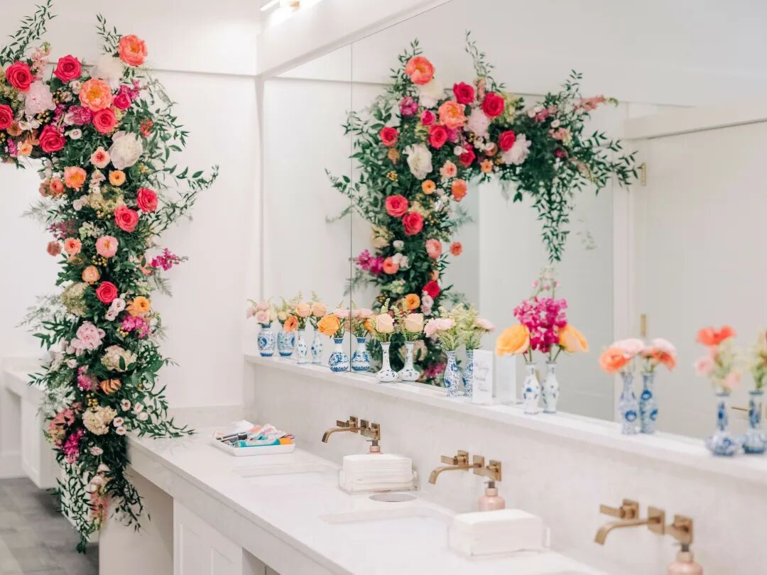 wedding venue bathroom decorated with pink flower arch, flowers in blue vases on the counter and small wedding bathroom basket